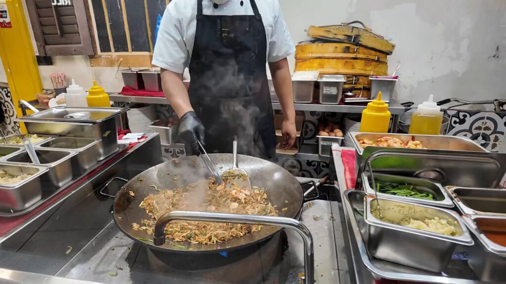 Cook tossing noodles in a wok at Signatures Food Court