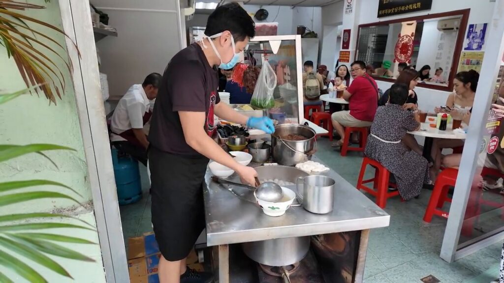 Busy noodle shop with sidewalk tables in Kuala Lumpur Chinatown