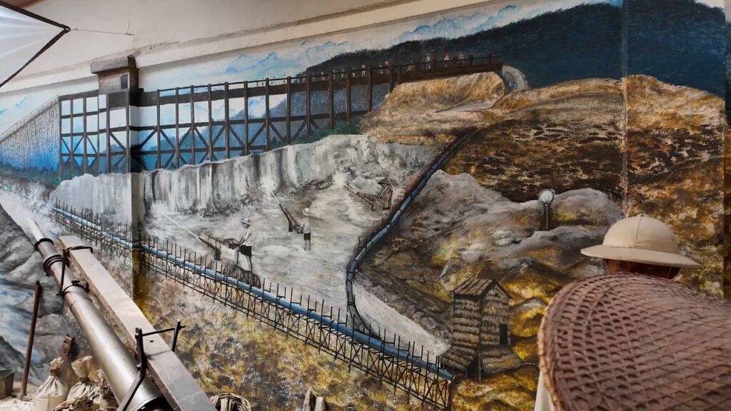 Guide explaining a tin mining mural at Han Chin Pet Soo
