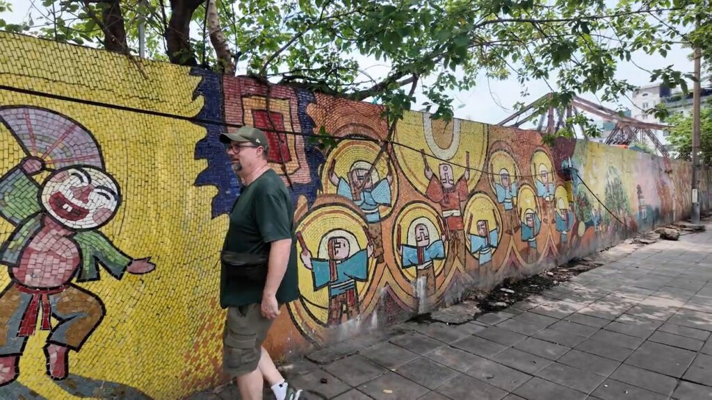 Bill walking beside a colorful section of the Hanoi mosaic mural