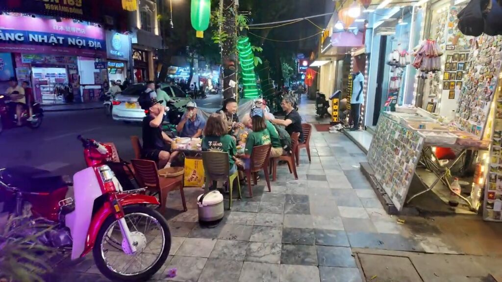 Locals sitting on small plastic stools on a Hanoi sidewalk at night