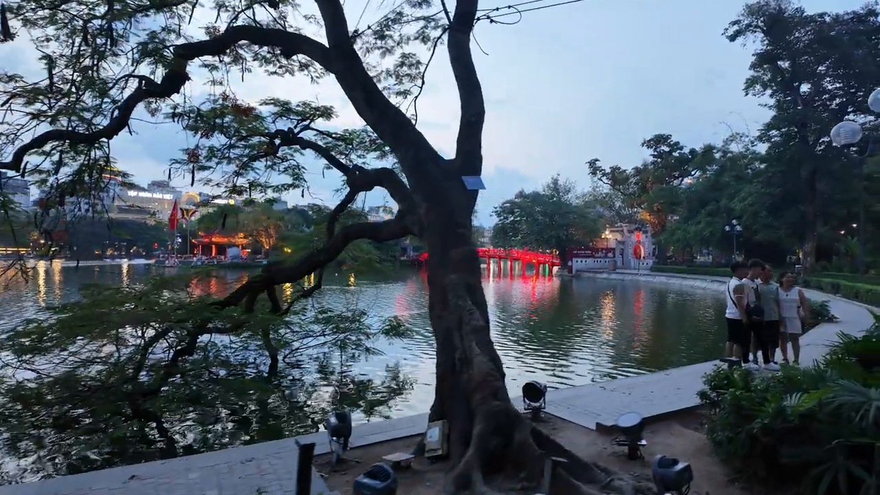 Tree over Hoan Kiem Lake with the red Huc Bridge at dusk in Hanoi